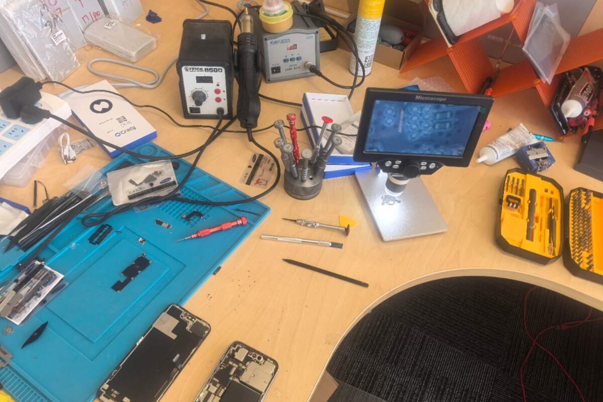 A device opened up on the DT Repair workbench beside a hot air rework station, soldering station and digital microscope