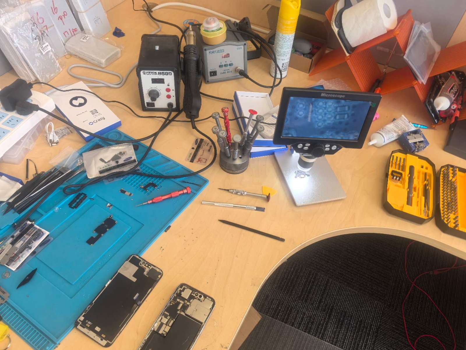 A device opened up on the DT Repair workbench beside a hot air rework station, soldering station and digital microscope